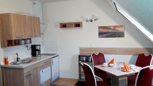 Une cuisine compacte équipée d’un évier, d’une machine à café et de placards. Un coin repas avec une table et des chaises est situé à côté de la cuisine.