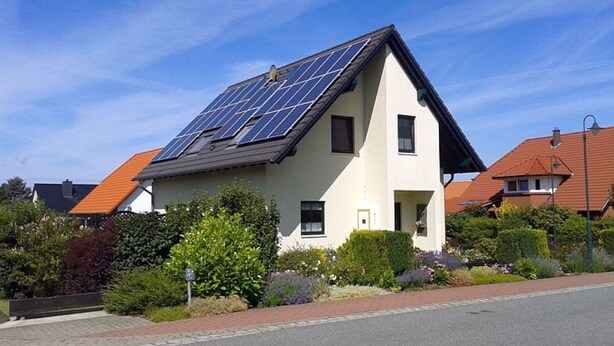 Une maison dotée de panneaux solaires sur le toit, entourée de verdure et sous un ciel dégagé.