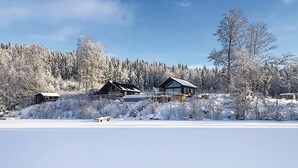Une cabane dotée d’une grande fenêtre, entourée d’arbres couverts de neige et surplombant un ciel dégagé.