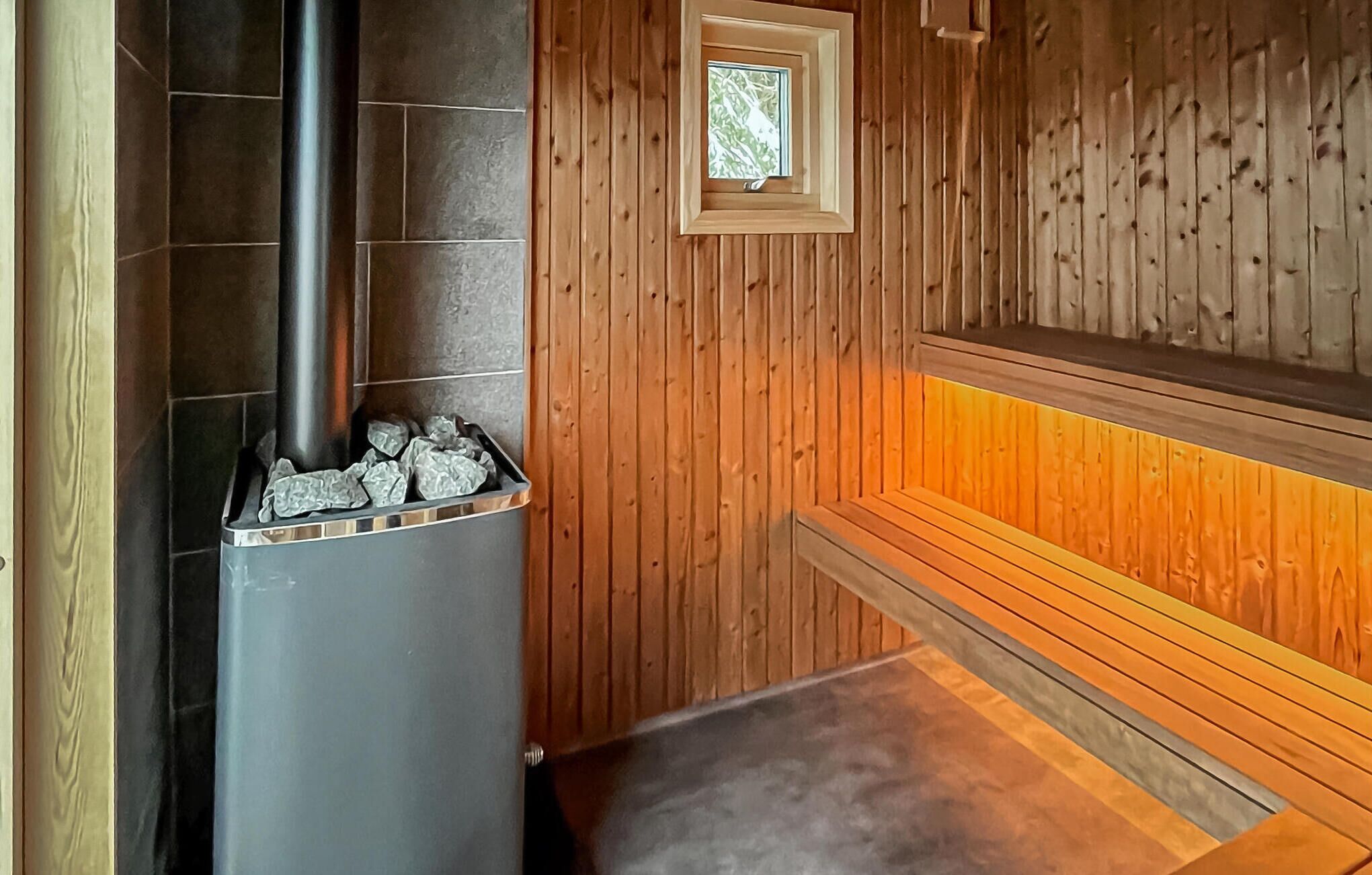 Un sauna avec un mur en pierre, un banc en bois et une petite fenêtre.