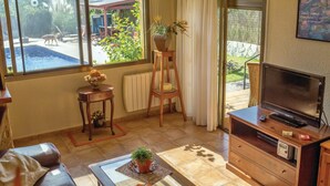 A cozy living room with a TV, wooden furniture, a small table with a plant, and a view of a swimming pool and garden. - Awesome home in Tordera (Tordera)