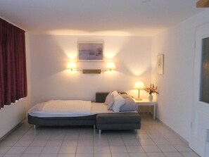 Een slaapkamer met een bed, nachtlampjes, een nachtkastje met een vaas, en een schilderij aan de muur.