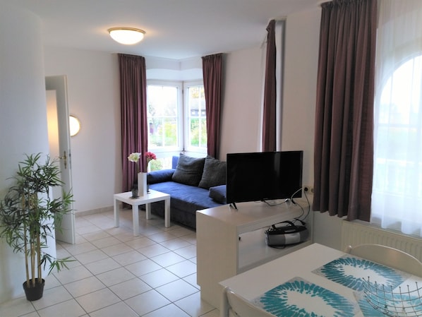 A modern living room with a flat-screen TV, a sofa, a small side table, and a potted plant.