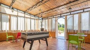 A room with a foosball table, green and red chairs, and a table with a view through large windows. - Lovely home in Dicomano FI with private swimming pool, can be inside or outside (Dicomano FI)