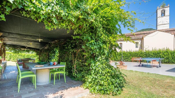An outdoor patio with a table and chairs, surrounded by lush greenery and a bell tower in the background. - Lovely home in Dicomano FI with private swimming pool, can be inside or outside (Dicomano FI)