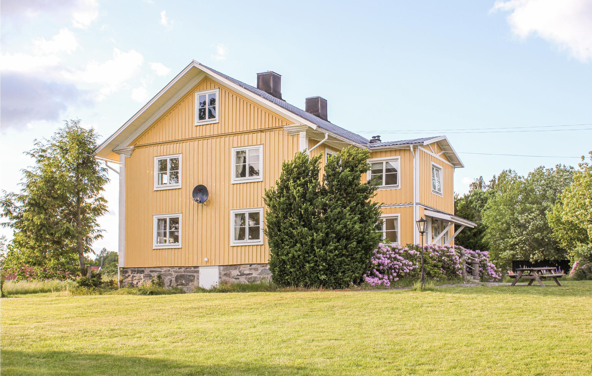 Ein gelbes Haus mit zwei Etagen, einem Steinuntergrund, zahlreichen Fenstern und einem großen Baum im Vorgarten.