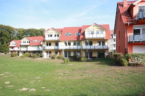 A row of multi-story buildings with balconies, a grassy courtyard, and a clear sky.