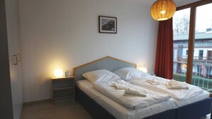 A bedroom with a bed, bedside lamps, a nightstand, a framed picture on the wall, and a window with curtains. - (57) 2-room apartment - apartment house Mecklenburg (Kühlungsborn)