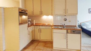 A compact kitchen with a built-in oven, a coffee maker, and a sink. - (57) 2-room apartment - apartment house Mecklenburg (Kühlungsborn)