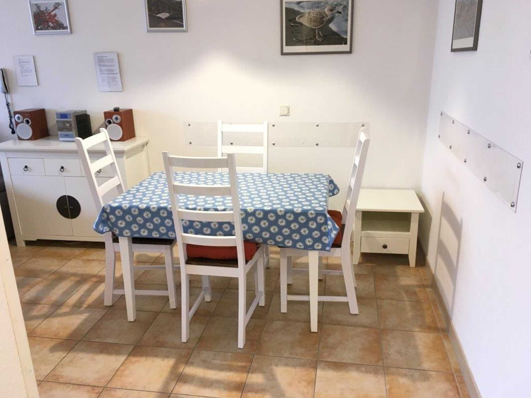 A small, clean room with a white table and chairs, a small cabinet, and a bed with a headboard.