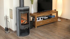 Ett vardagsrum med en vedeldad kamin, en platt-TV, en möbel i trä för förvaring av underhållningsutrustning och en golvlampa.
