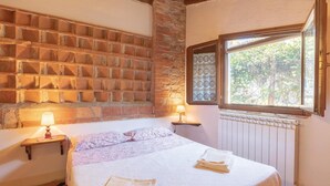 A bedroom with a brick wall, a window with a view of trees, a bed with a white bedspread, and two bedside lamps. - Nice home in S.Vito In Monte TR (S.Vito In Monte TR)