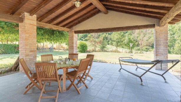 An outdoor patio with a wooden table and chairs, a basketball hoop, and a covered area with a view of a garden and trees. - Nice home in S.Vito In Monte TR (S.Vito In Monte TR)
