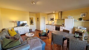 A compact living space with a sofa, coffee table, dining table, and chairs. A kitchen area with cabinets, microwave, and stove is visible. - (261) 2-room apartment-Hafenstraße - Apartment holiday dreams (Kühlungsborn)