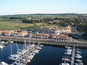 Un port de plaisance où sont amarrés de nombreux bateaux, un ensemble de bâtiments situés au bord de l’eau et une végétation luxuriante environnante.