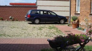A car parked in a driveway with a brick building and a small garden area. - Fw 1 - 69364 - FW1 - 69364 (Malchow)