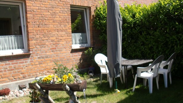 A brick house with a patio area featuring a wooden bench, potted plants, and outdoor furniture. - Fw 1 - 69364 - FW1 - 69364 (Malchow)