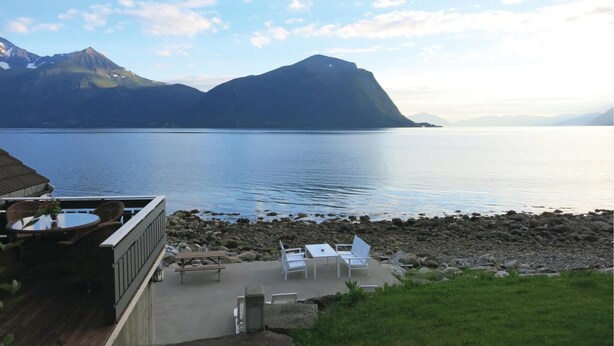 A lakeside view with a deck area featuring outdoor seating and a view of mountains in the background. - Amazing home in Hundeidvik with ethernet internet (Hundeidvik)