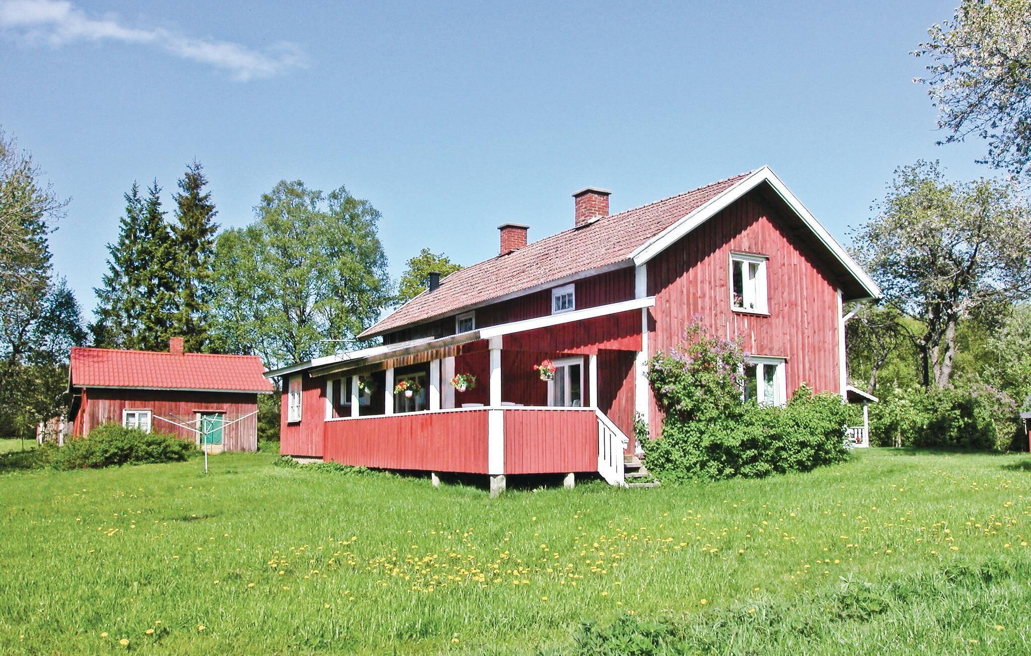 A red wooden house with a porch, surrounded by green grass and trees.