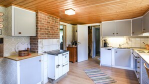 A compact kitchen with wooden ceiling beams, white cabinets, a brick wall, and a small window.