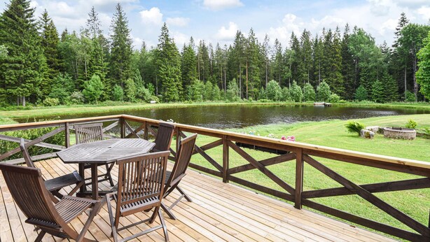 A wooden deck with a table and chairs overlooking a lake, surrounded by dense forest.