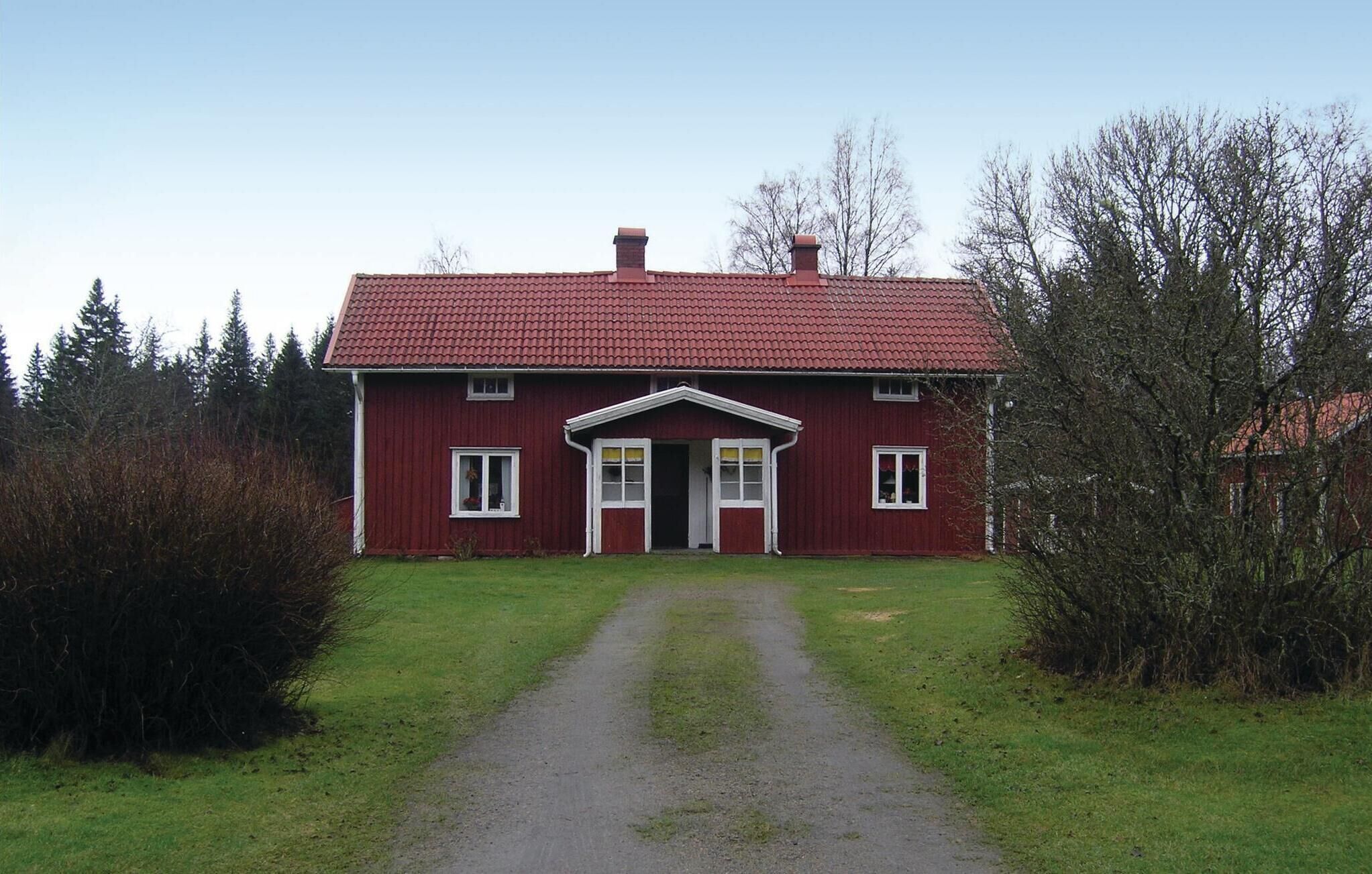 Une maison rouge à deux étages, dotée d’une façade symétrique, d’une entrée centrale avec un petit porche et d’une allée en gravier menant à la porte d’entrée.