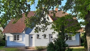 A white house with a tiled roof, a brick pathway, and a small bush in the foreground. - Apartment 1 / o. l -. Rügen-Fewo 47 (Putbus)