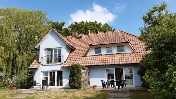 A two-story house with a tiled roof, a balcony, and a small patio area with outdoor furniture. - Apartment 1 / o. l -. Rügen-Fewo 47 (Putbus)