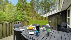 An outdoor dining area with a table set for two, surrounded by wicker chairs, a potted plant, and a coffee pot. - Awesome home in Brovst with sauna (Brovst)