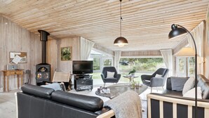 A cozy living room with a wooden ceiling, a black leather sofa, a TV, and a fireplace. - Awesome home in Brovst with sauna (Brovst)