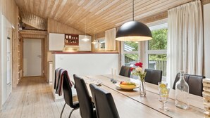 A modern kitchen with wooden cabinets, a dining area with a wooden table and chairs, and a large window with curtains. - Awesome home in Brovst with sauna (Brovst)