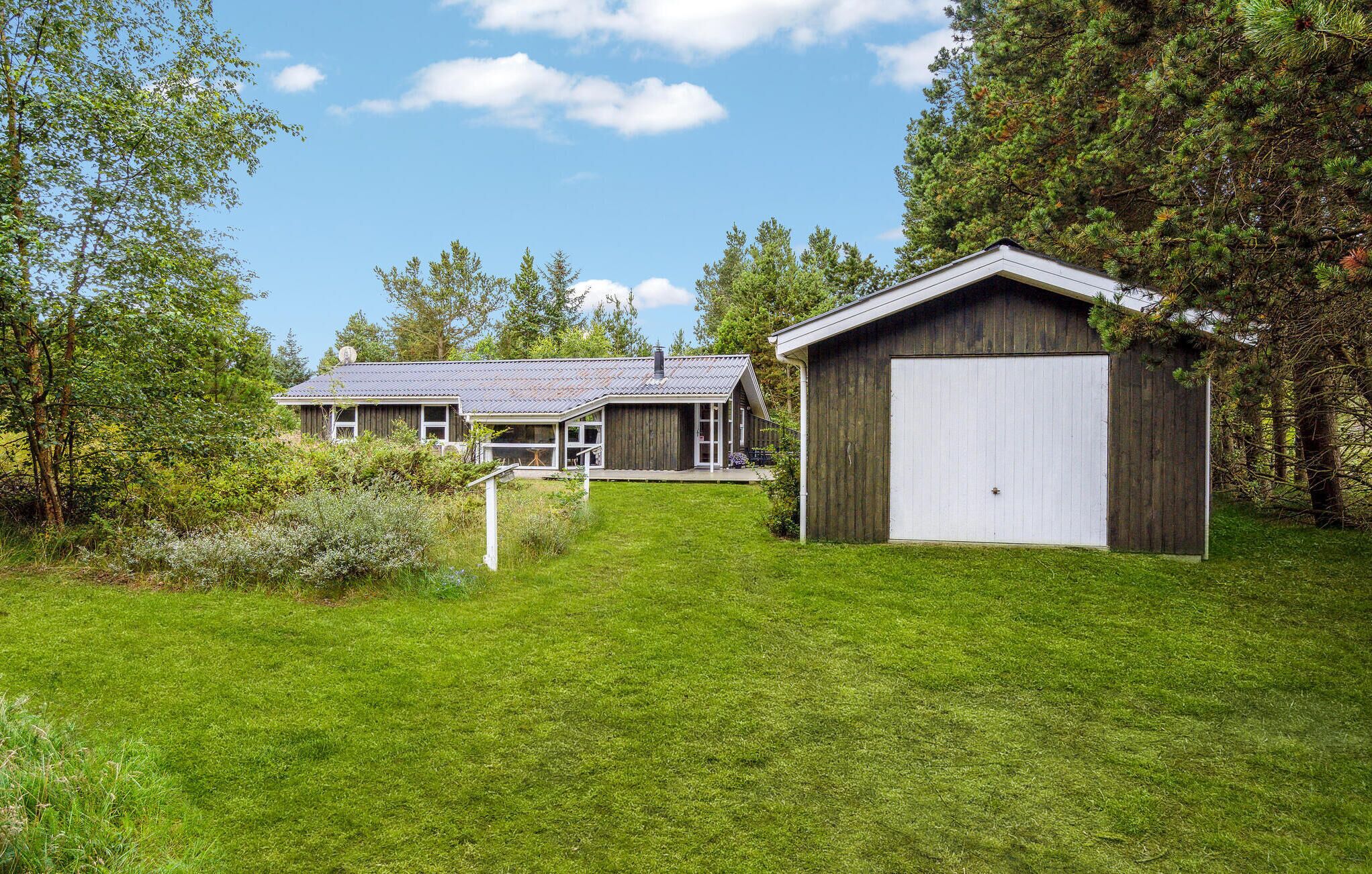 Eine rustikale Holzhütte mit einer großen Garage, umgeben von üppiger Vegetation und Bäumen.