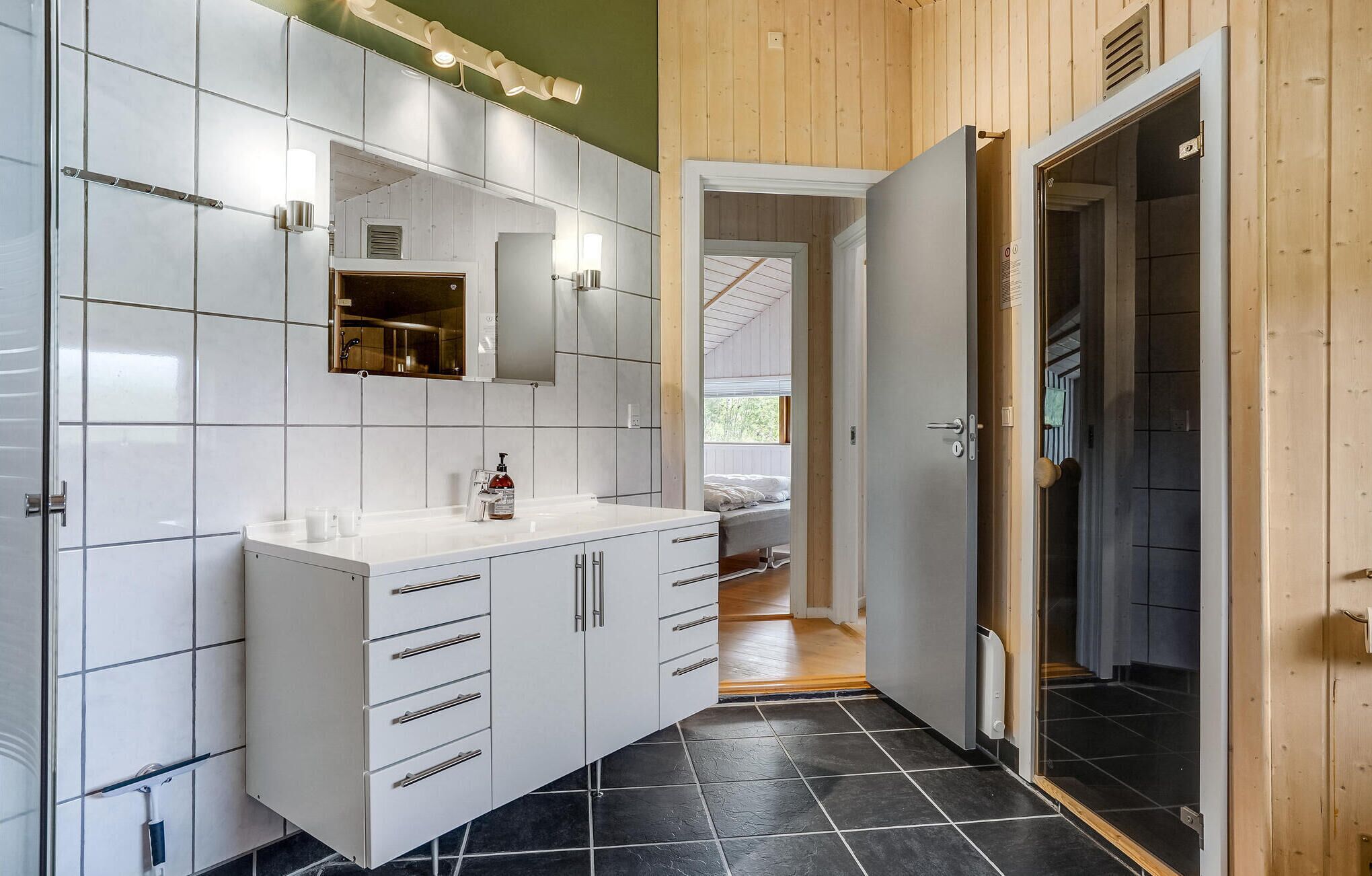 Et moderne badeværelse med hvide skabe, et stort spejl og et sort flisegulv.