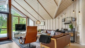 A modern living room with a leather sofa, a dining area with a laptop, and a large window offering a view of the outdoors. - Amazing home in Glesborg with sauna (Glesborg)