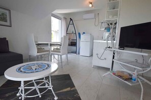 Een moderne woonkamer met een eethoek, een televisie, een koelkast en een wit kastje.