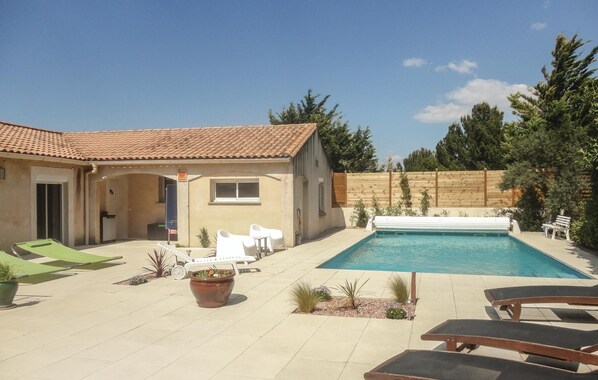 Un jardin avec une piscine, des chaises longues et un petit bâtiment doté d’un toit en tuiles.