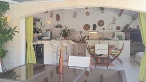 A compact kitchen with a dining area, featuring a central island, bar stools, and a glass-top table. - Amazing home in Nebian (Nebian)