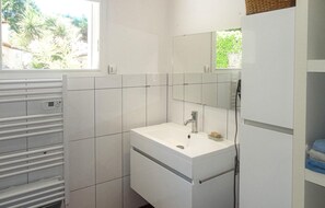 Une salle de bain moderne avec des carreaux blancs, un lavabo avec un miroir et une fenêtre donnant sur un espace verdoyant.