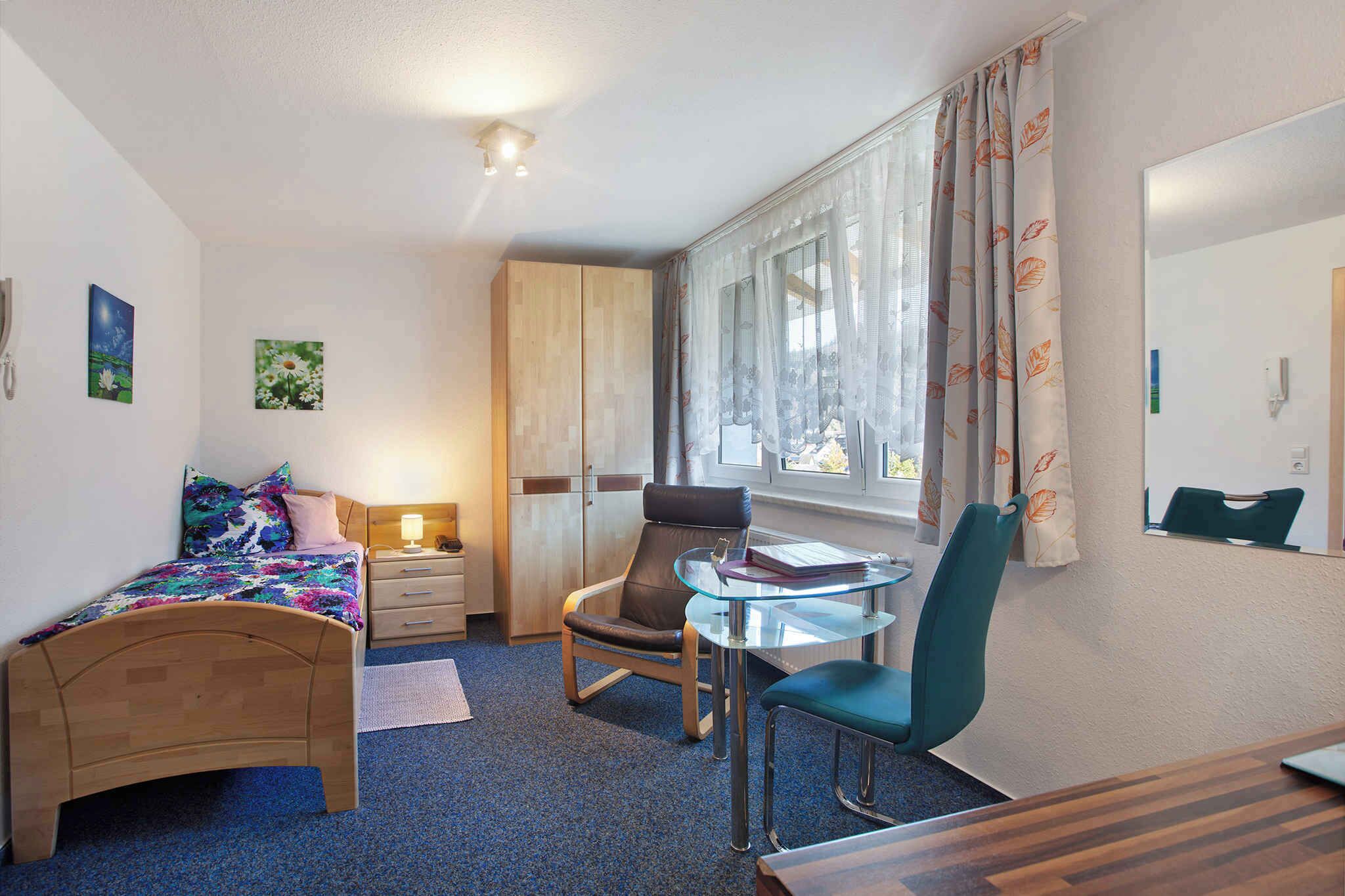 A bedroom with a bed, a desk, a chair, a mirror, and a window with curtains.