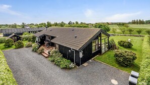 Une grande maison moderne, dotée d’un toit en pente, entourée d’une pelouse bien entretenue et avec un terrain de golf en arrière-plan.
