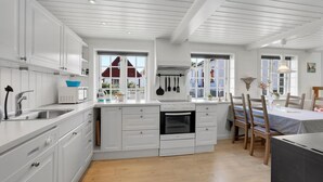 A modern kitchen with white cabinetry, a built-in oven, and a dining area with wooden chairs and a table. - 1 bedroom gorgeous apartment in Svaneke (Svaneke)