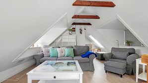A modern loft apartment with a sloped ceiling, a grey sofa set, a white coffee table, and a wooden beam ceiling. - 1 bedroom gorgeous apartment in Svaneke (Svaneke)