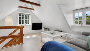 A modern, well-lit room with a sloped ceiling, a flat-screen TV, a coffee table, and a sofa. - 1 bedroom gorgeous apartment in Svaneke (Svaneke)