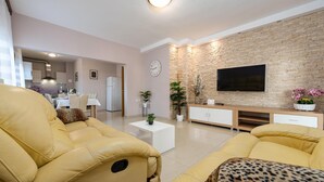 Una sala de estar moderna con sofás amarillos, un televisor de pantalla plana, una pared de piedra y un comedor al fondo.