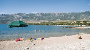 Una playa con una sombrilla verde, gente tomando el sol y montañas al fondo.