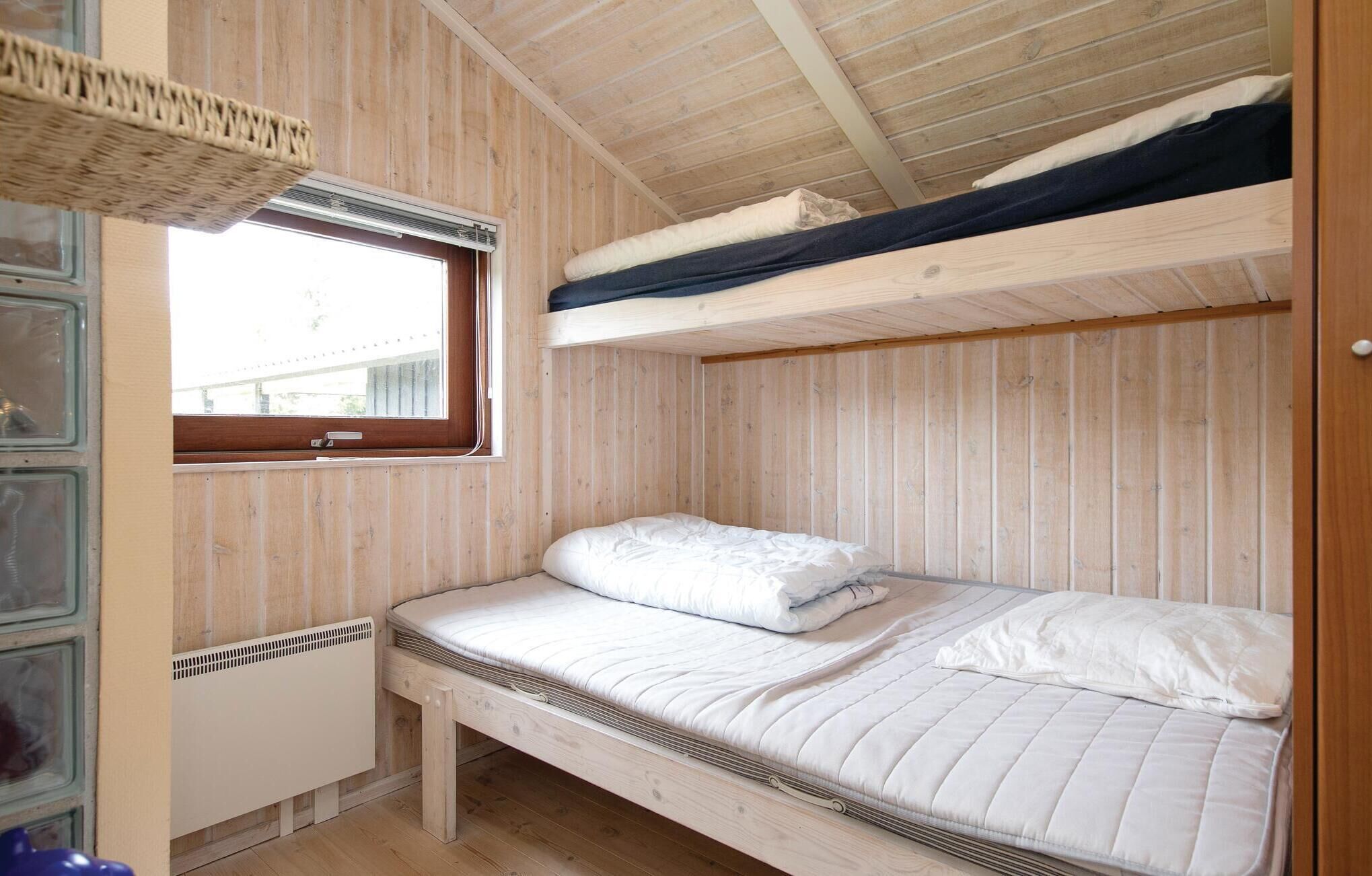A wooden cabin room with a bunk bed, a single bed, a window, and a radiator.