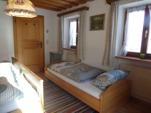 Une petite pièce agréable, dotée d’un lit simple, d’une porte en bois, d’un radiateur et d’une fenêtre avec des rideaux.