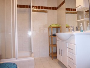 Une salle de bain avec une douche, un lavabo avec un miroir et une étagère en bois où sont posées des serviettes.