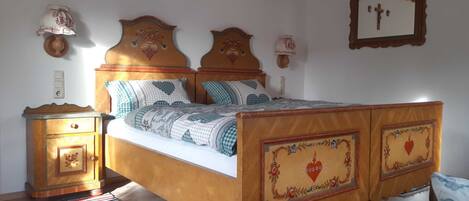 A bedroom with a wooden bed, a nightstand, a wall-mounted cross, and a framed picture.