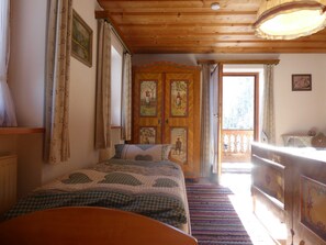 Une chambre avec un plafond en bois, un lit recouvert d’une courtepointe à carreaux, une armoire en bois et une fenêtre avec des rideaux.